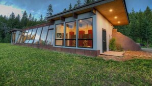 Un bâtiment moderne doté de grandes fenêtres et d’un toit en pente, entouré d’une pelouse et d’arbres.
