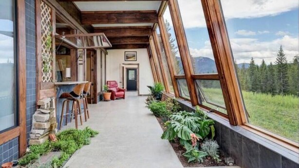 Un couloir extérieur abrité, doté de poutres en bois, de plantes en pot et offrant une vue sur un paysage montagneux.