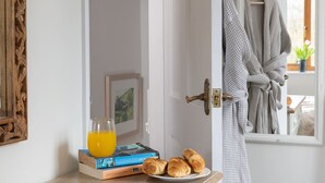 A room with a wooden door, a framed picture, a glass of orange juice, books, and croissants on a plate. - A stone cottage that sleeps 4 guests in 2 bedrooms (Combe Martin)
