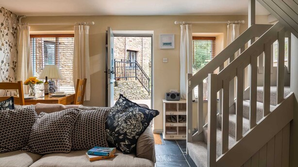 A living room with a sofa, a coffee table, a lamp, and a bookshelf. There is a staircase leading to an upper level. - Bantam Cottage - sleeps 2 guests  in 1 bedroom (Combe Martin)