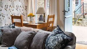A cozy living room with a sofa, two chairs, a table with a vase of flowers, and a lamp. - Bantam Cottage - sleeps 2 guests  in 1 bedroom (Combe Martin)