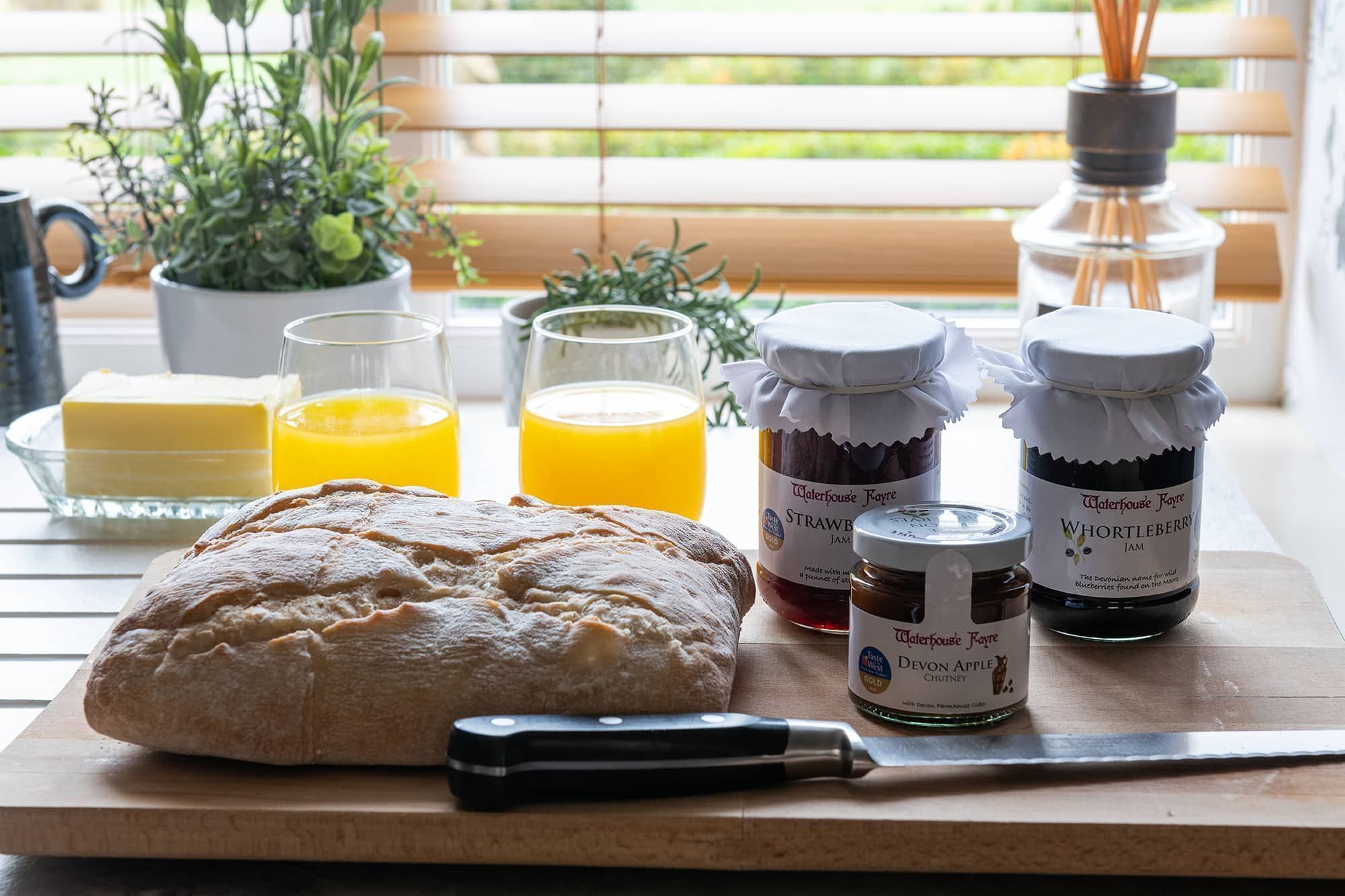 Ein Frühstückstisch mit Brot, Butter, Orangensaft, Marmelade und Chutney.