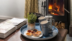 A cozy room with a wood-burning stove, a tray with tea cups and jam-filled tarts, a potted plant, and a stack of magazines. - A stone cottage that sleeps 3 guests  in 1 bedroom (Combe Martin)