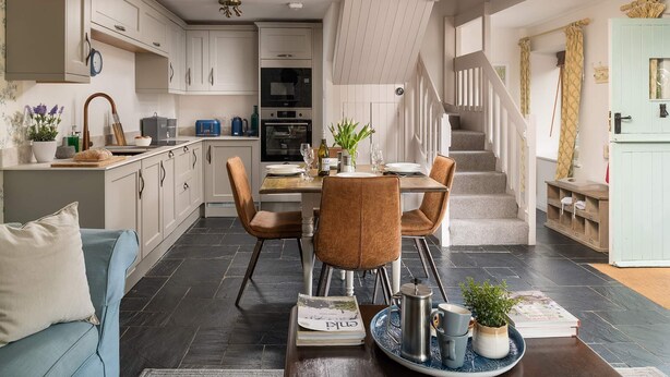 A modern kitchen with white cabinets, a dining area with a table set for four, and a staircase leading to an upper level. - A stone cottage that sleeps 3 guests  in 1 bedroom (Combe Martin)