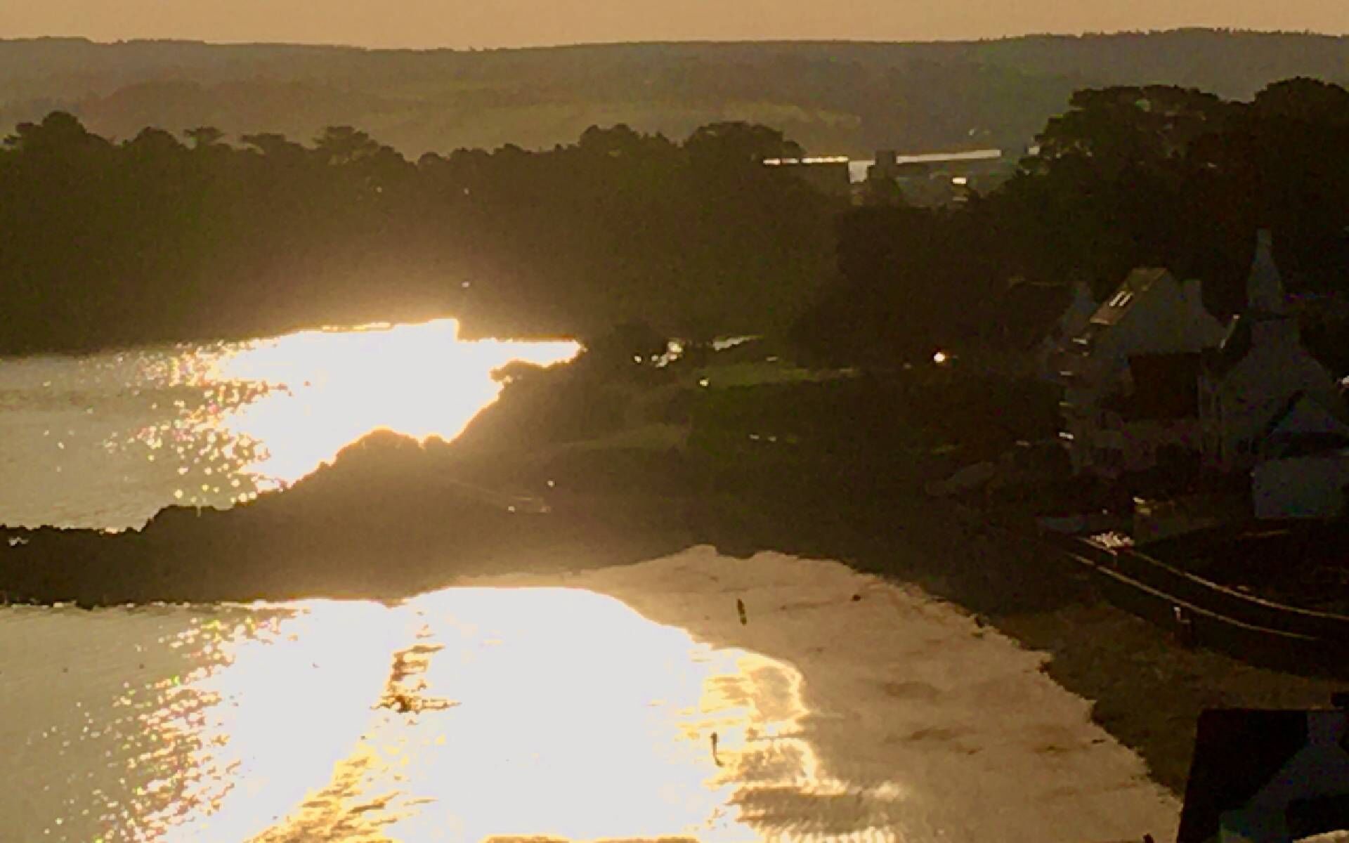 Solnedgang over vand med en bro i baggrunden.
