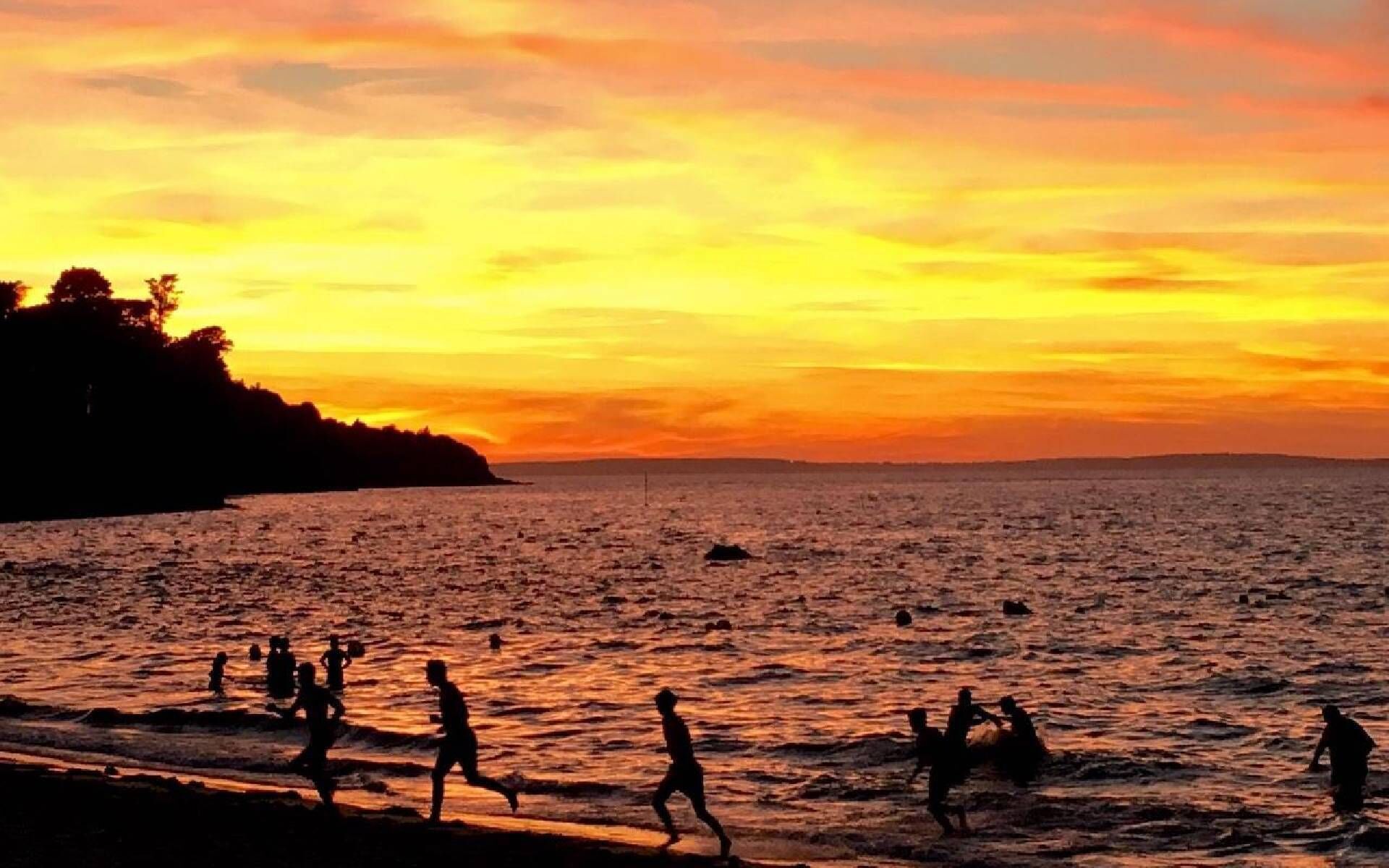 A beach scene with people walking along the shore during sunset.