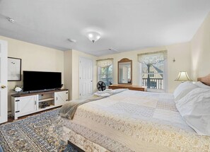 A bedroom with a large bed, a television on a stand, a fan, and a window with a view.