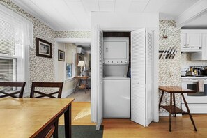 A compact kitchen with white cabinetry, a dining area with a wooden table and chairs, and a small seating area with a lamp.