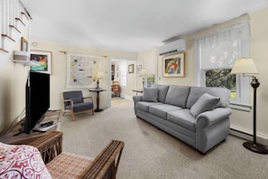 Una sala de estar con un sofá gris, un televisor, un sillón de mimbre y una lámpara.