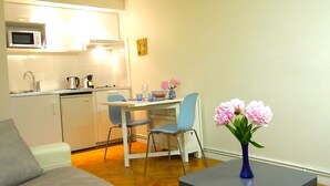 A compact living space with a kitchenette, a dining area, and a seating area with a sofa and a table with flowers.