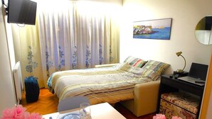 A hotel room with a bed, a desk with a chair, a TV, a desk lamp, and a painting on the wall.