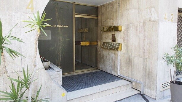 A building entrance with a glass door, a metal gate, and a small step leading up to the entrance.