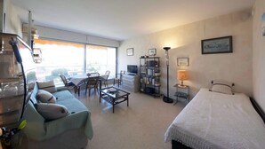 A well-lit living room with a sofa, coffee table, TV, bookshelf, and a bed. - Nice studio on the seafront (Arcachon)