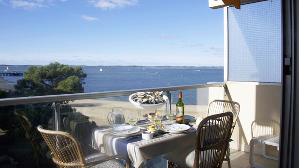 A balcony with a table set for dining, overlooking a body of water with boats. - Nice studio on the seafront (Arcachon)