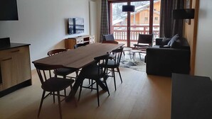 Moderni olohuone, jossa on puinen ruokapöytä, tuoleja, sohva ja televisio.