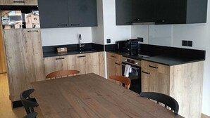 Moderni keittiö, jossa on puinen ruokapöytä, mustat kaapit ja suuri musta televisio, joka on asennettu työtason yläpuolelle.