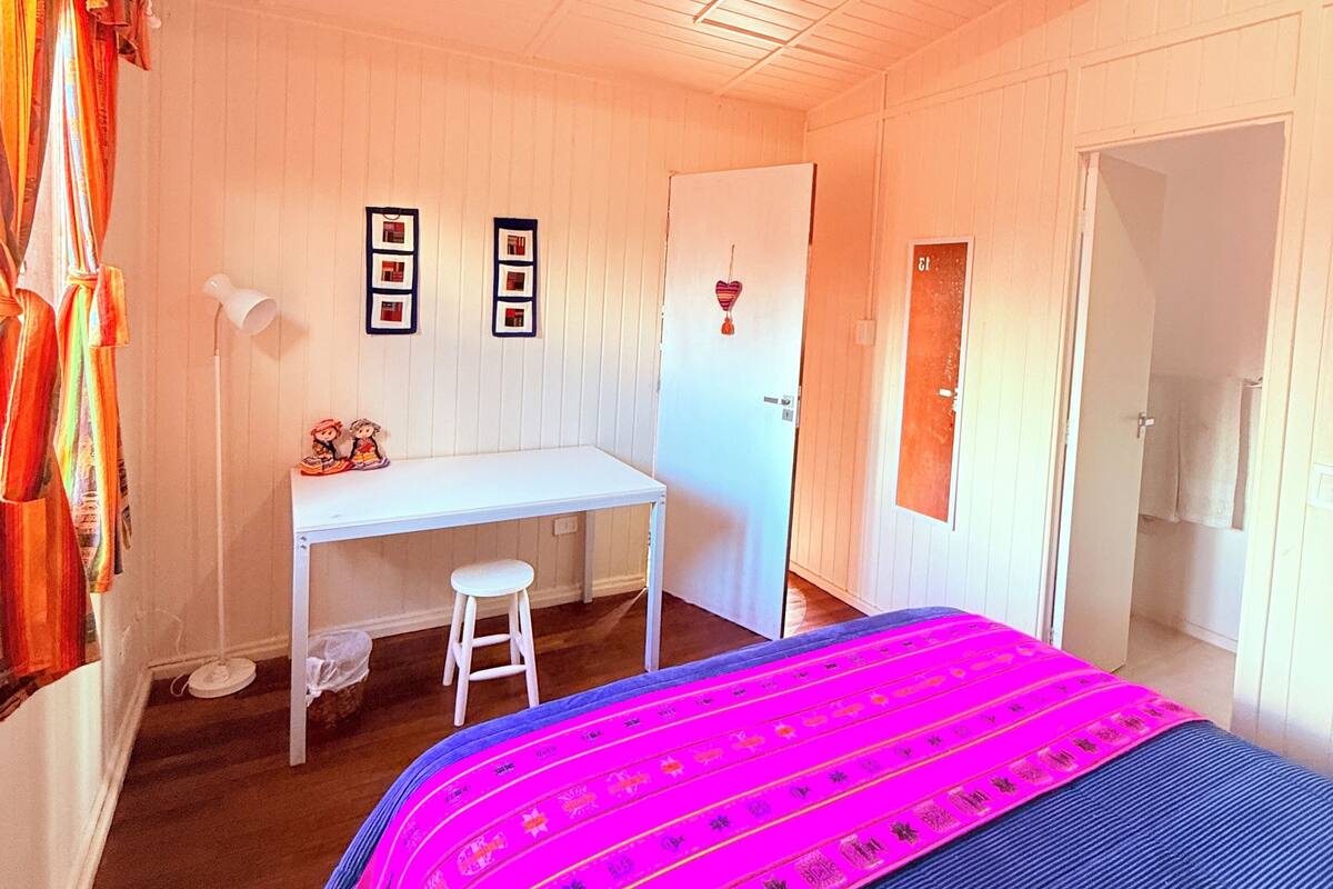 Ein Schlafzimmer mit Bett, Schreibtisch und Stuhl. Eine Tür und ein Fenster sind vorhanden.