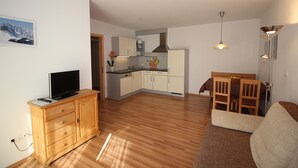 Un espace de vie compact comprenant un meuble en bois, un téléviseur, un coin repas avec une table et des chaises, et une cuisine équipée de meubles et d’une cuisinière.