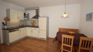 Une cuisine compacte avec des meubles blancs, un plan de travail en bois et un coin repas comprenant une table et des chaises marron.