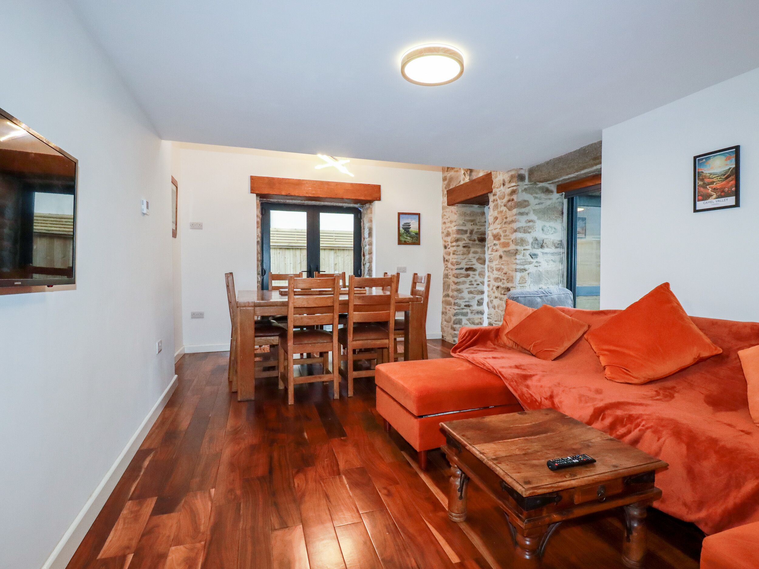 Un salon avec une table à manger en bois, un canapé orange et un mur en pierre.