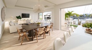 Un salon moderne avec une table à manger en bois, des canapés blancs et une grande fenêtre donnant sur une marina.