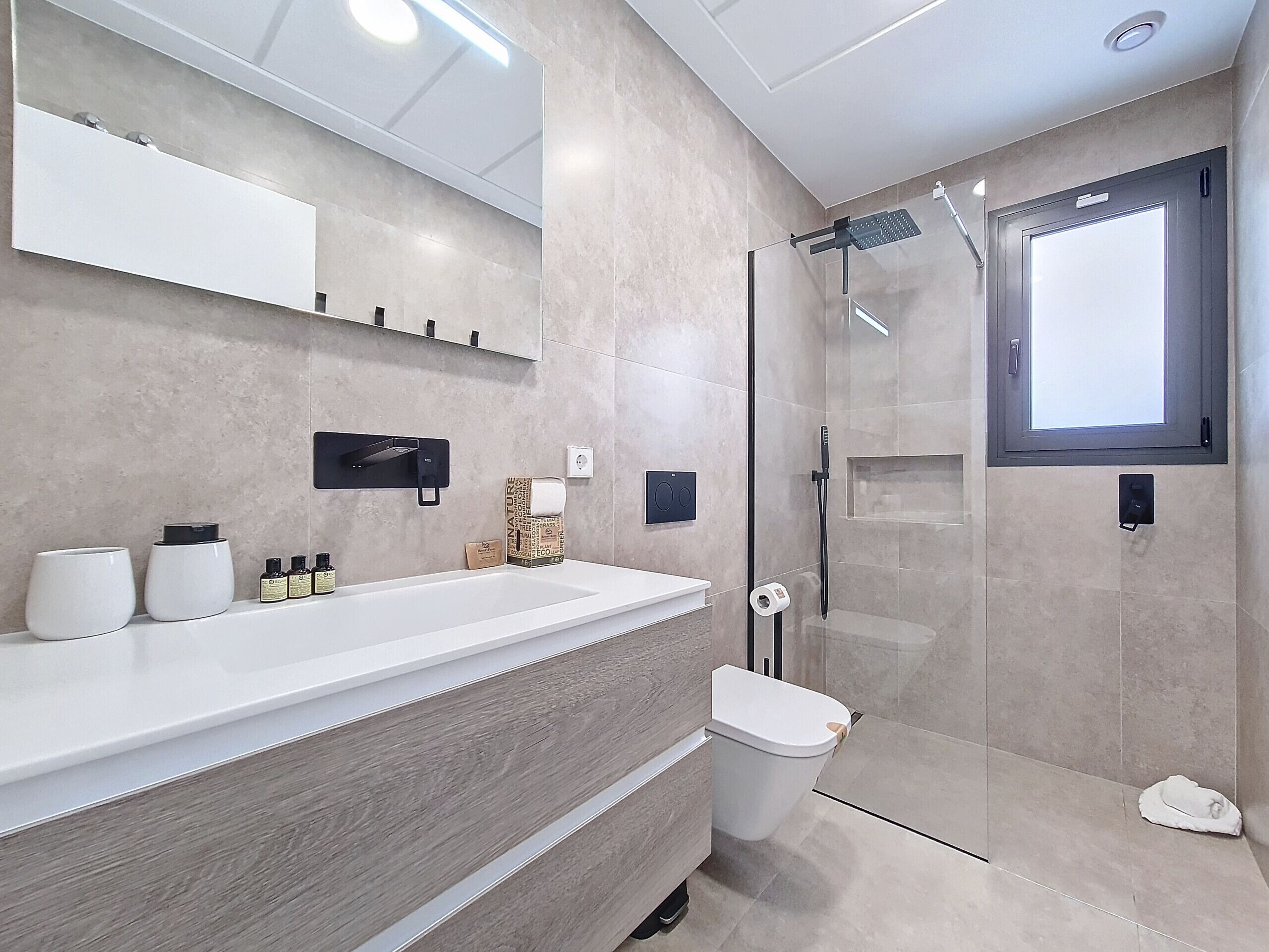 A modern bathroom with a large mirror, a white sink, a glass shower enclosure, and a toilet.