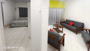 A living room with a sofa set, a small table, and a bed with patterned bedding.