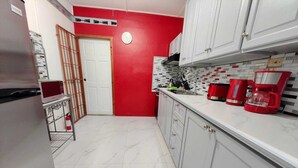 A kitchen with white cabinets, a red wall, and a tiled backsplash.