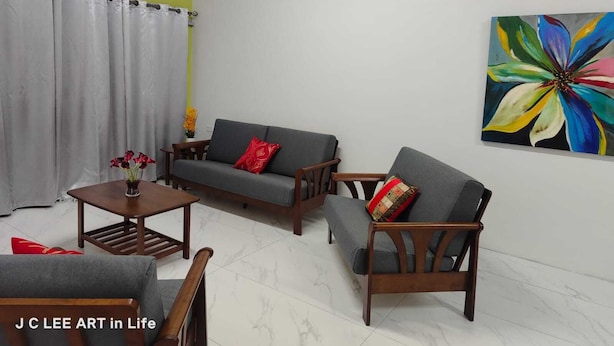 A living room with a grey sofa, a wooden coffee table, and a red and yellow patterned pillow. A colorful flower painting is on the wall.