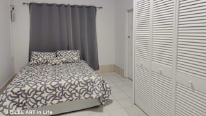 A bedroom with a bed, grey curtains, and a white wardrobe.