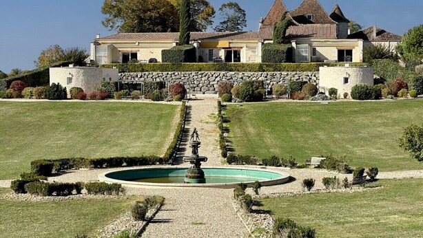 A large estate with a central fountain, symmetrical landscaping, and a prominent building with multiple towers.
