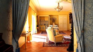 A spacious living room with a yellow armchair, a chandelier, and a view of a kitchen and dining area through an archway.