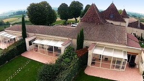 A large estate with multiple buildings, including a main house with a steeply pitched roof and several smaller structures. There are well-maintained lawns and hedges, and the estate is surrounded by open fields and trees.