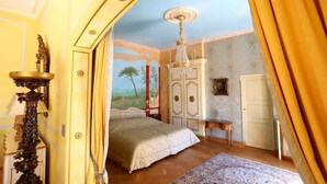 A bedroom with a bed, a chandelier, a wardrobe, and a painting on the wall.
