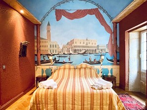 Hotellihuone, jossa on sänky, yöpöytä ja seinämaalaus, jossa on esitetty kaupunkimaisema.