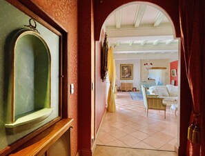 Un couloir mène à un salon où se trouvent un canapé blanc, un tapis à motifs et un tableau accroché au mur.