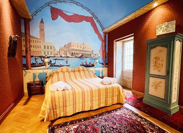 Ein Hotelzimmer mit einem Bett, einem Nachttisch, einer großen Wandteppich mit Stadtansicht, einem grünen Schrank und einem Teppich mit Muster.