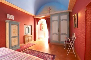 A bedroom with a large bed, a wardrobe, and a mirror. There is a door leading to another room.