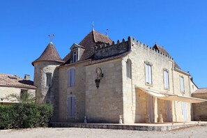 A historic stone building with a tower, a covered entrance, and a small garden area.