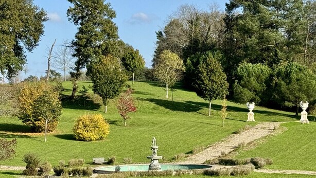 A well-maintained garden with a fountain, pathways, and various trees.