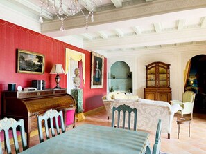 Ein Zimmer mit roter Wand, einem Holztisch, einem Tisch und Stühlen. Es gibt eine Chandelier, einen Schrank und ein Gemälde an der Wand.