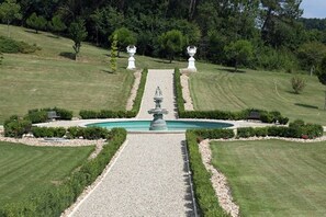 Ein formal gestalteter Garten mit einem zentralen Brunnen, symmetrischen Wegen und gepflegten Rasenflächen.