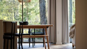Ein moderner Essbereich mit einem Holztisch und -stühlen, einer hängenden Leuchte und Blick auf Bäume durch große Fenster.