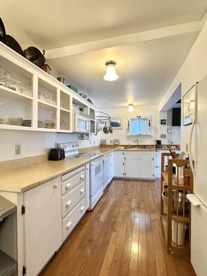Una cocina con armarios blancos, encimera de madera, estufa y lavaplatos.
