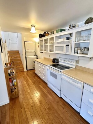 Cocina con piso de madera, muebles blancos, estufa, microondas y refrigerador.