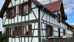 A two-story traditional half-timbered house with a red-tiled roof, a fenced yard, and a street view.