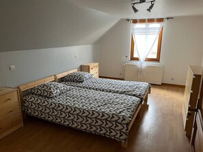 Ein Schlafzimmer mit zwei Betten, einem Fenster mit Vorhängen, einem Heizkörper und Holzmöbeln.