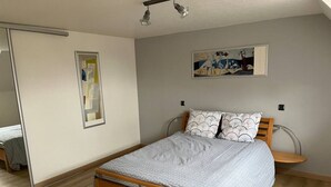 A bedroom with a wooden bed, a bedside table, a mirror, and a wall-mounted artwork.