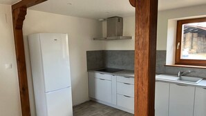 A kitchen with white cabinets, a white refrigerator, a wooden beam structure, a window with a view of outdoor barrels, and a stainless steel sink.