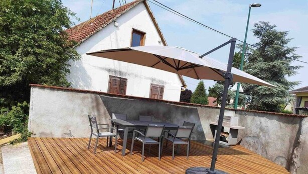 An outdoor wooden deck with a table and chairs, a large umbrella, and a barbecue grill.